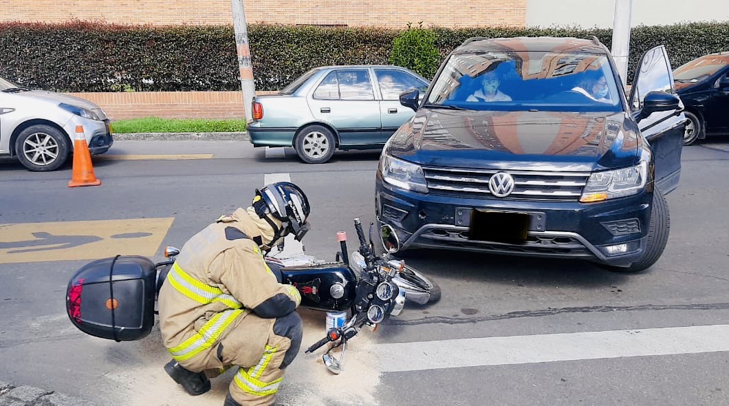 Bombero arrodillado revisando una moto acostada que colisiono con vehículo 